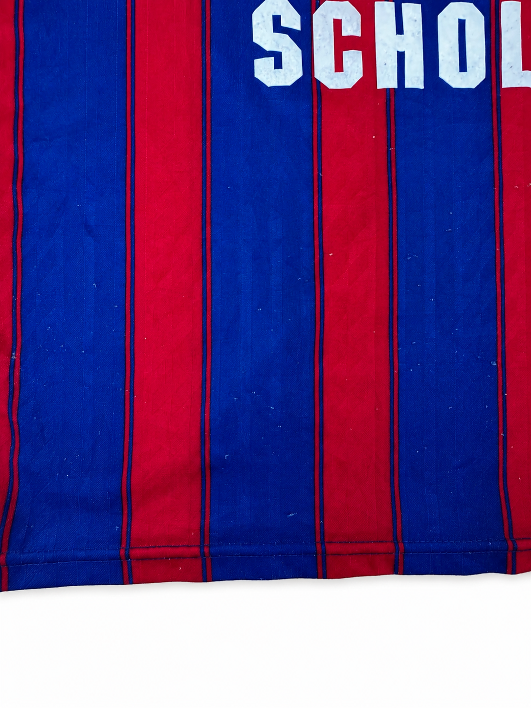 Close-up of a striped sports jersey with vertical red and blue stripes and white lettering reading 'SCHOL' at the top.