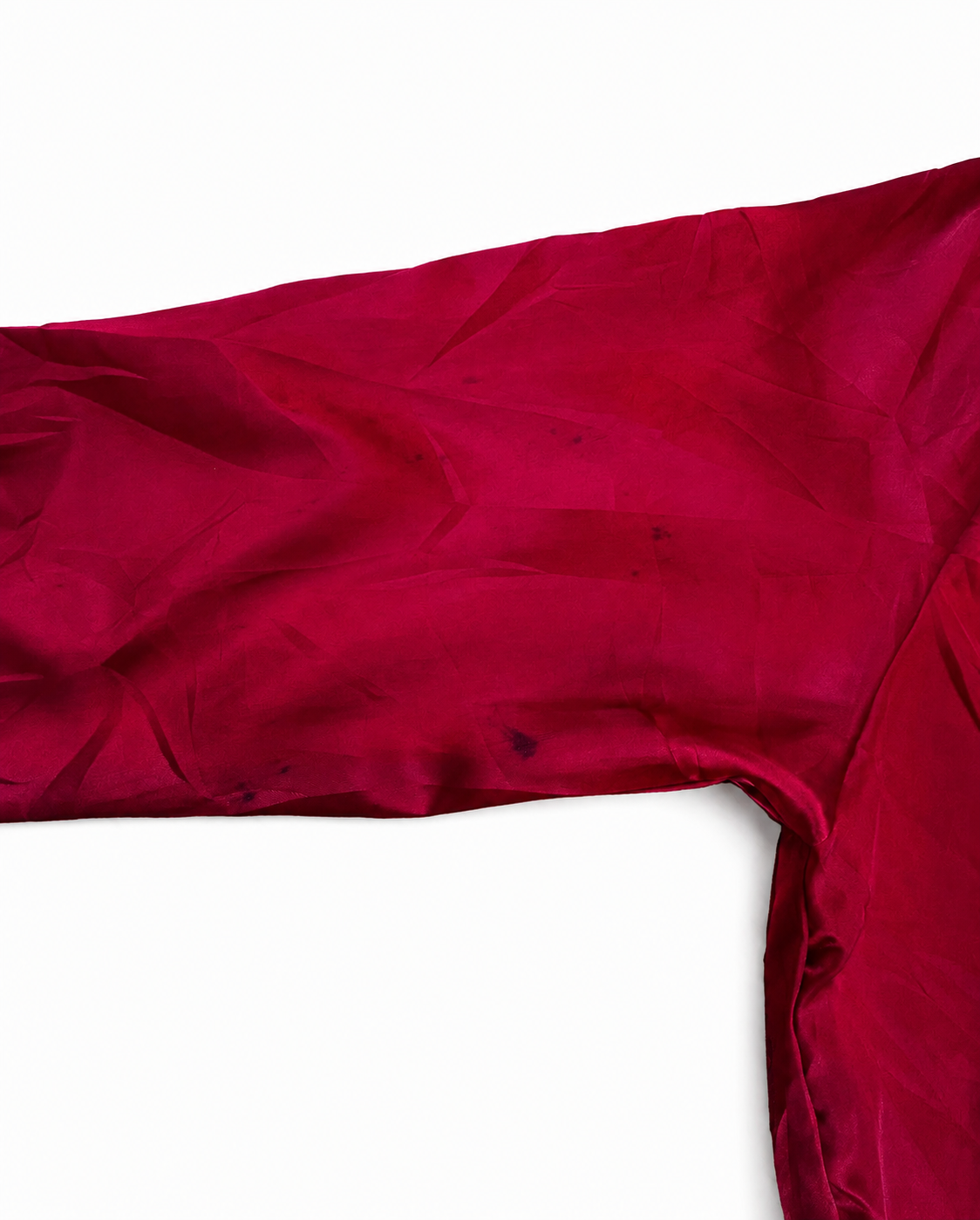 A close-up of a deep red fabric, likely a satin or silk garment sleeve, draped against a plain white background.