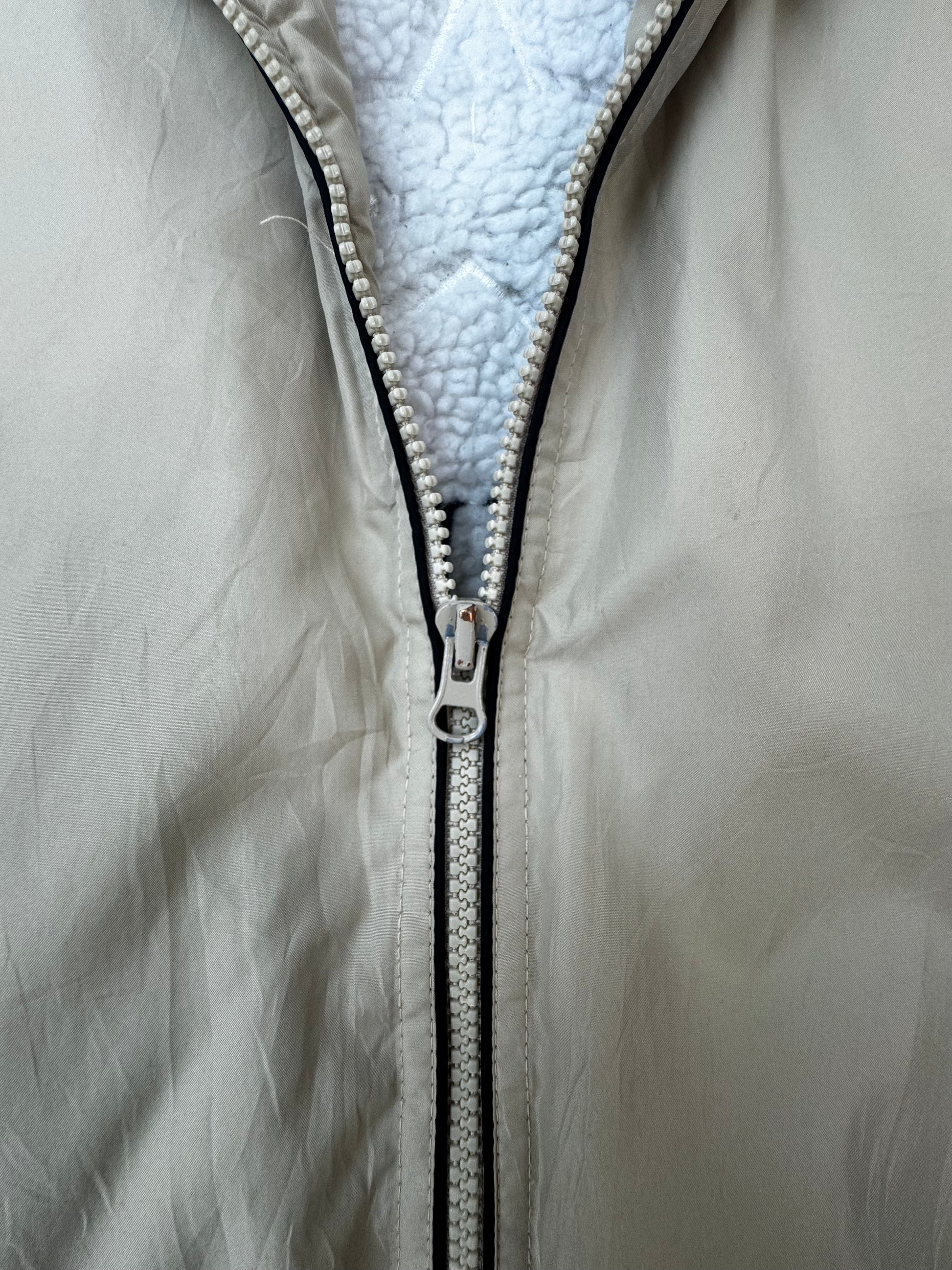 Close-up of a light beige or off-white zippered jacket with a white sherpa lining visible along the open front.
