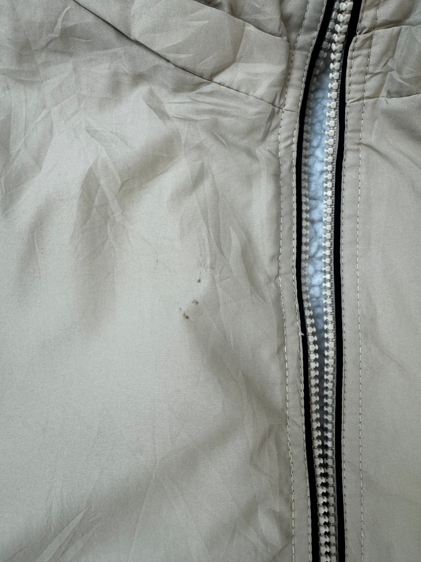 Close-up of a light tan jacket fabric with a black zipper, showing some wrinkles and a small stain on the surface.