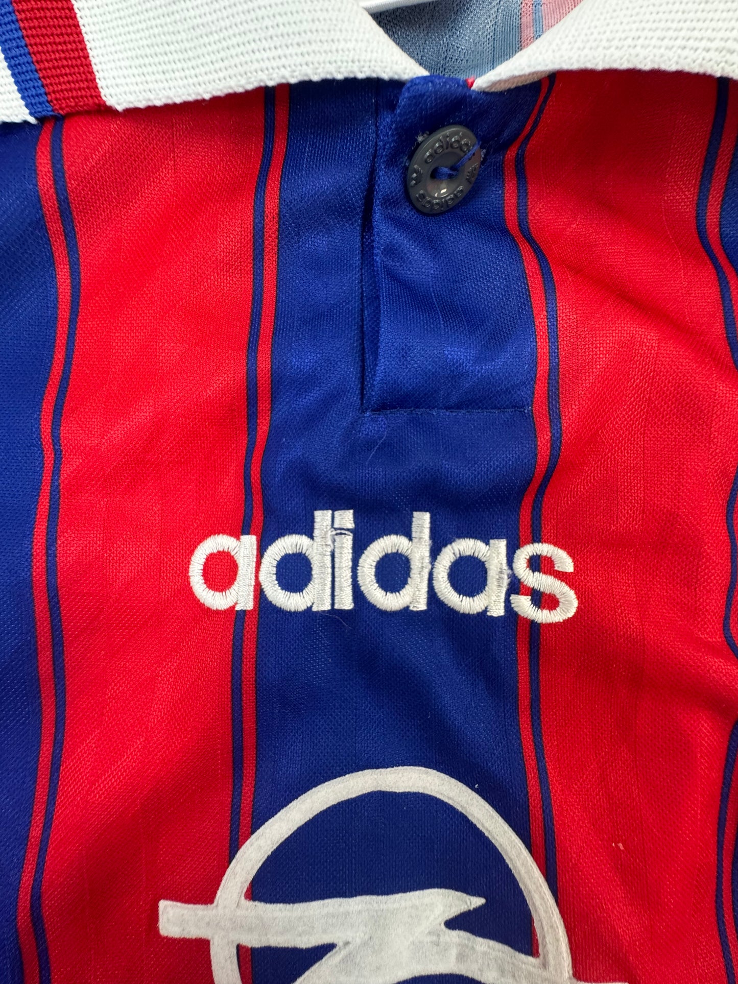 Close-up of a red and blue striped Adidas polo shirt with a white collar and white embroidered logo.