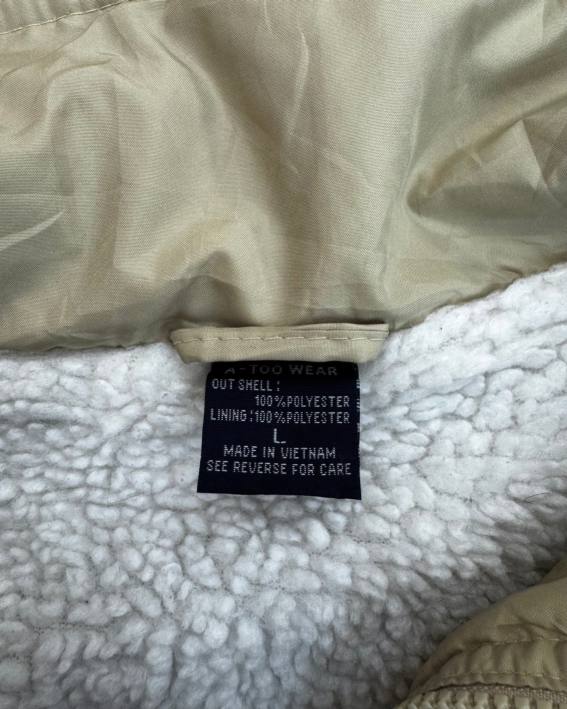Close-up of a garment interior showing a beige nylon shell lining and a white sherpa fleece lining, with a black sewn-in size tag reading 'A 100 WEAR' and material details.