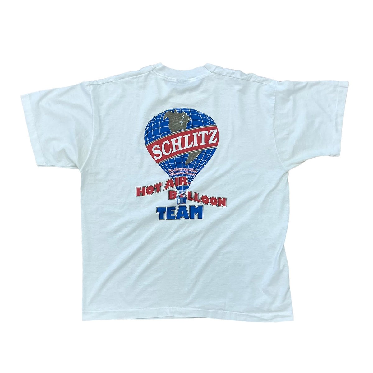 BACK SIDE. HOT AIR BALLOON IN BLUE WITH SCHLITZ WRITTEN IN RED AND WHITE ON IT. SAYS HOT AIR BALLOON TEAM